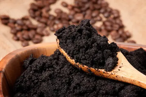 En skopa kaffesump i en träskål, redo för komposten. I bakgrunden syns rostade kaffebönor.