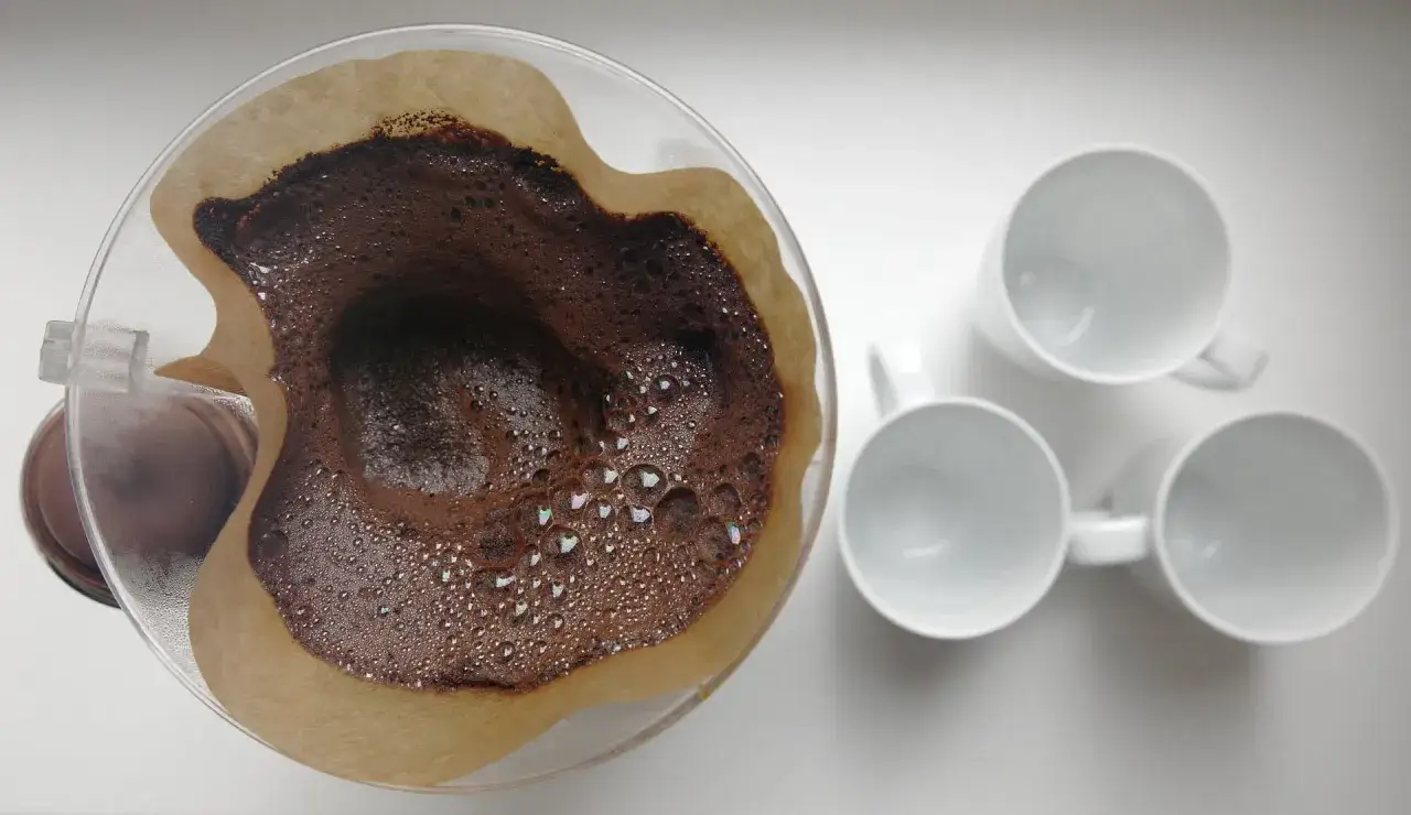 F&auml;rskt kaffe bryggs i ett filter, redo att serveras i tre vita muggar. Kaffesumpen ser ut att vara perfekt f&ouml;r att torka och &aring;teranv&auml;nda.